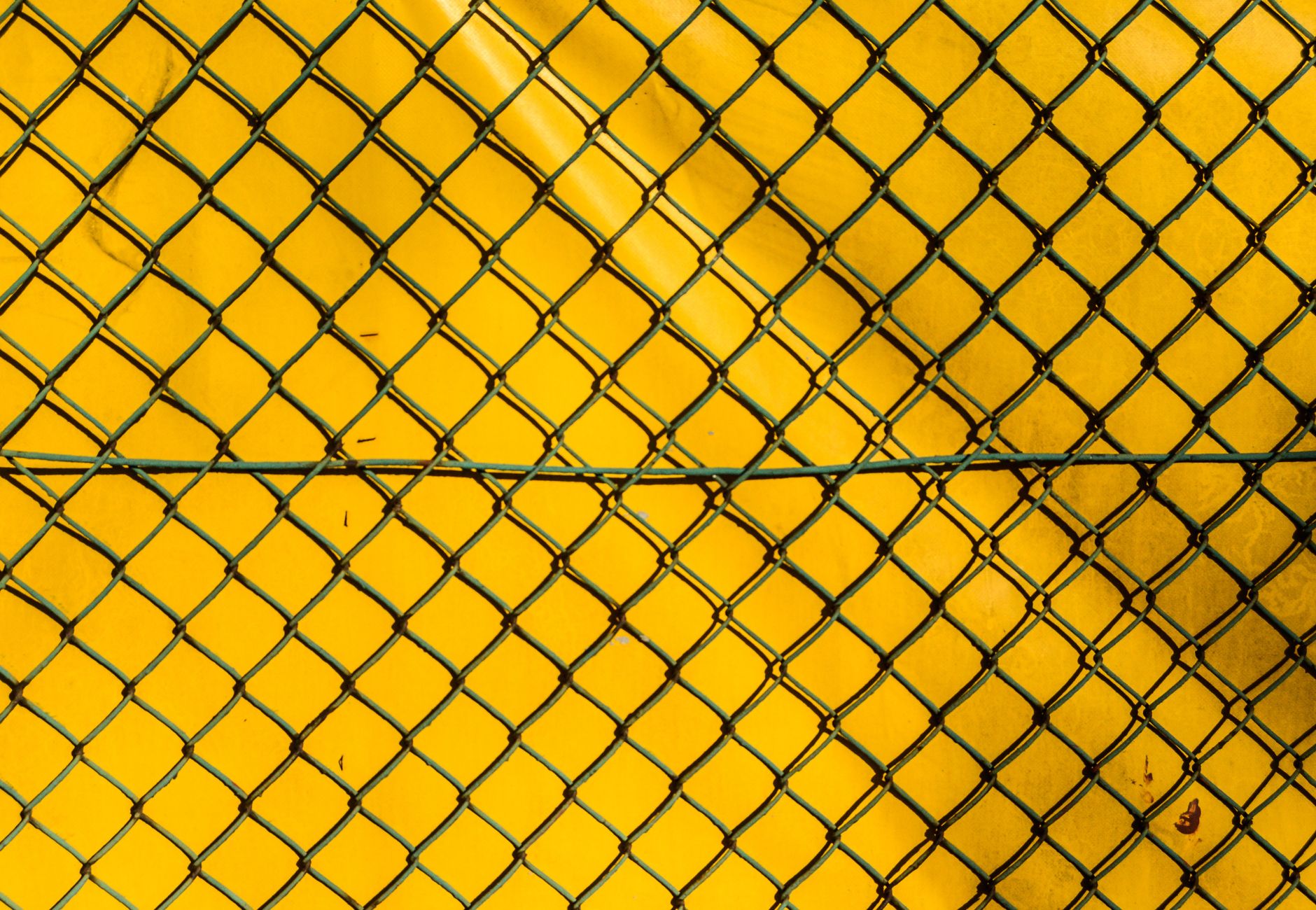 A close-up of a chain link fence against a bright yellow background, creating a stark contrast.
