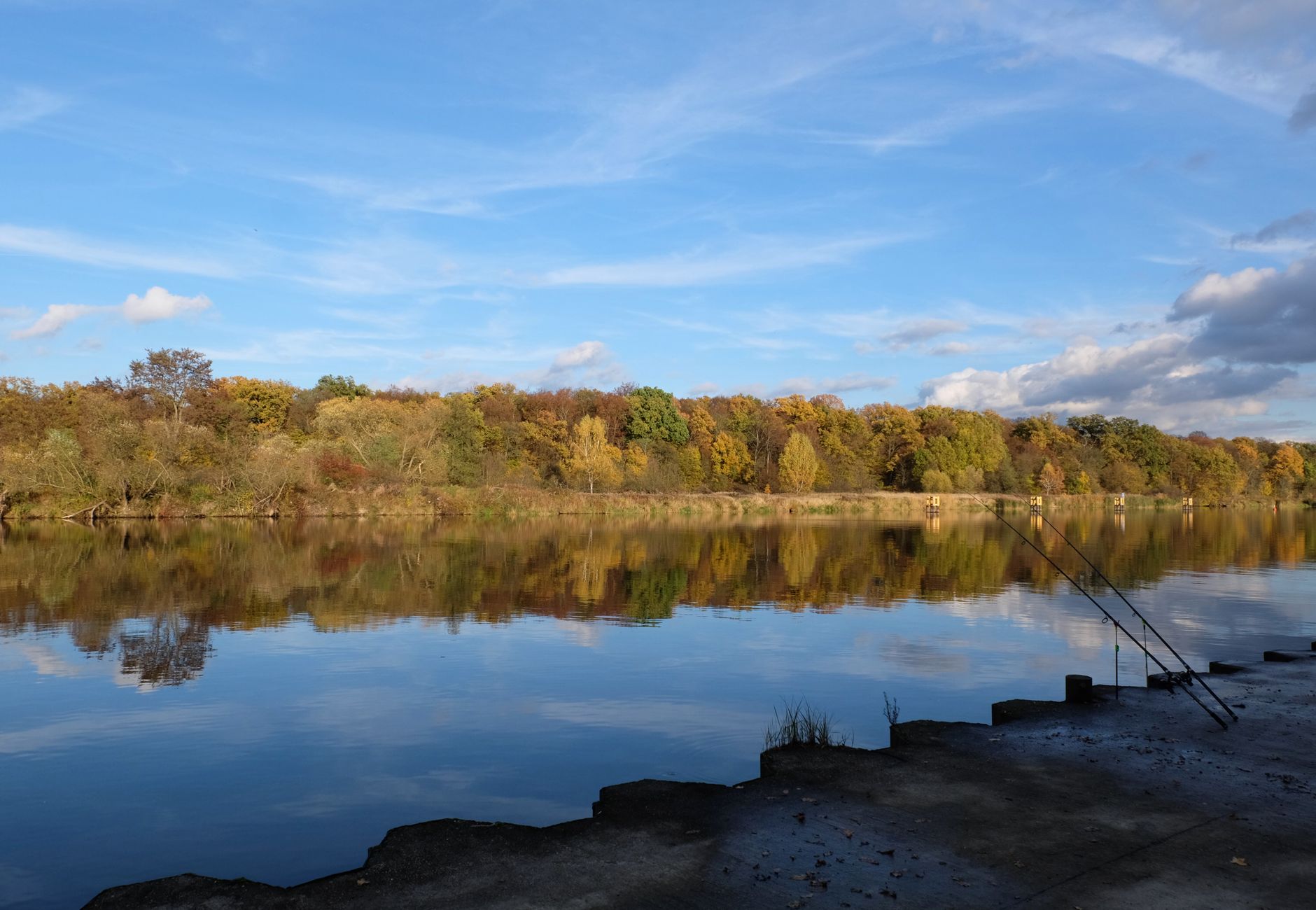 Peaceful autumn scene of a river with fishing rods under a clear blue sky.