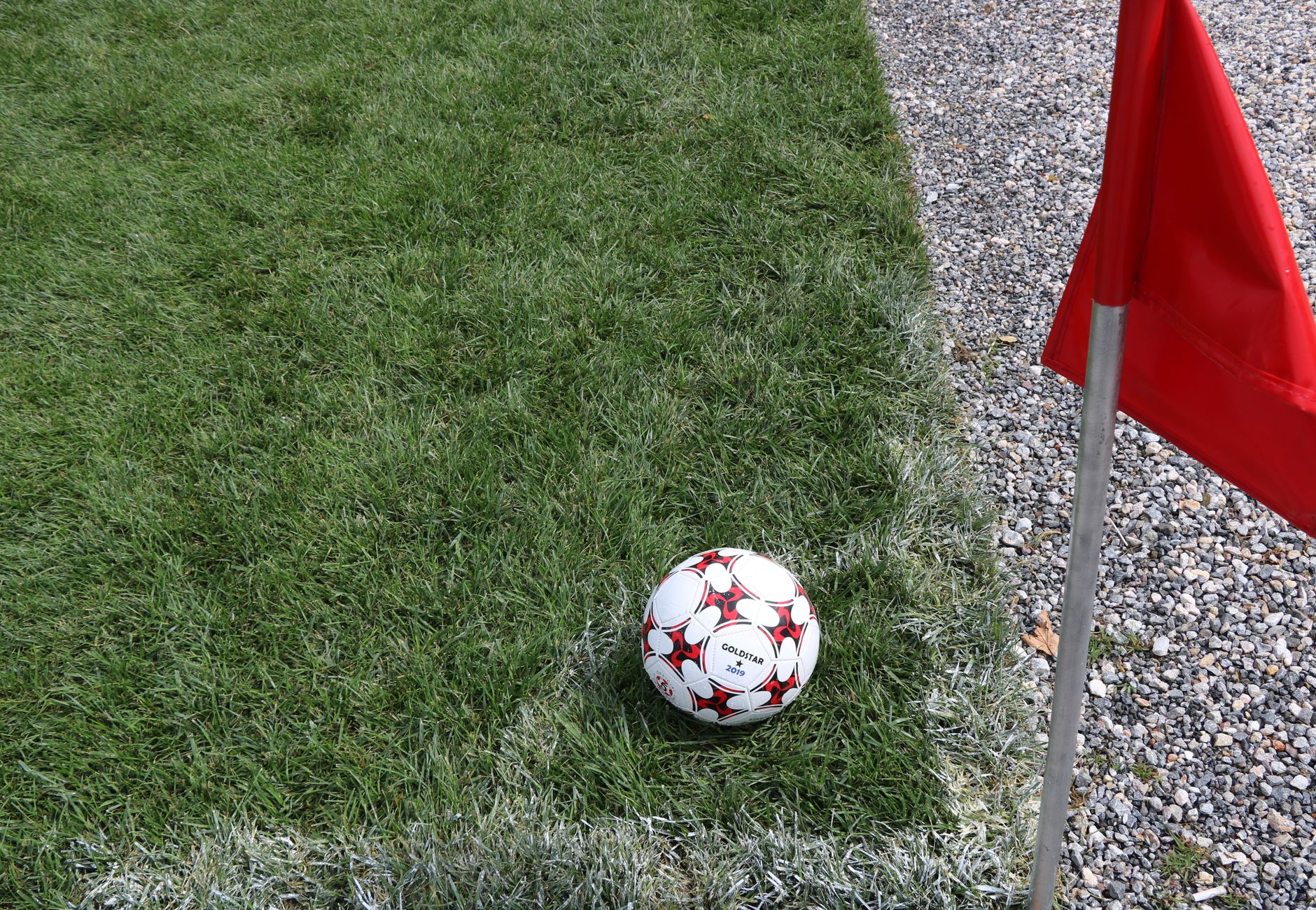 A close-up of a soccer ball near a red corner flag on a grass field, ideal for sports themes.