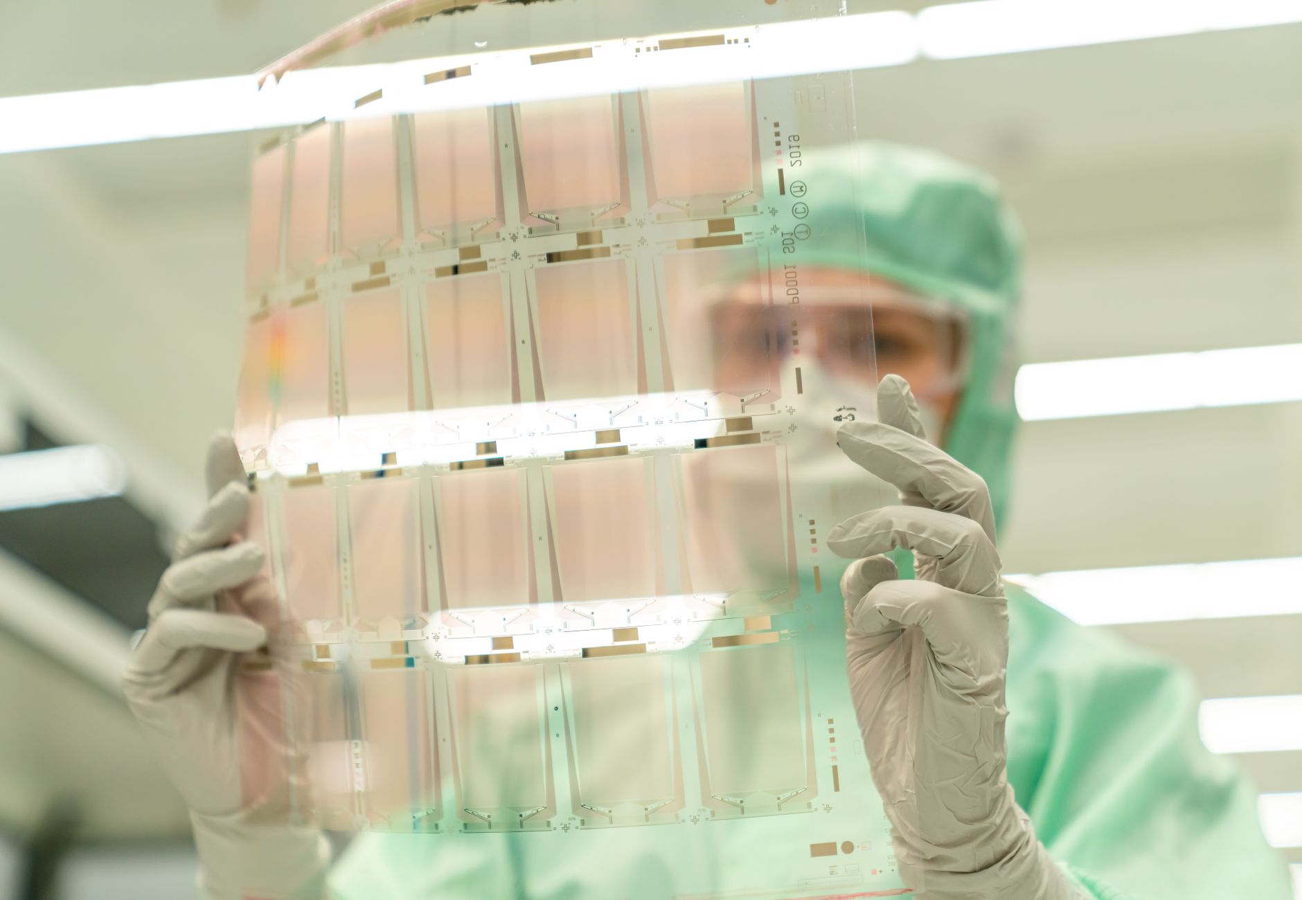 Scientist in protective gear holding a transparent test sheet in a laboratory.