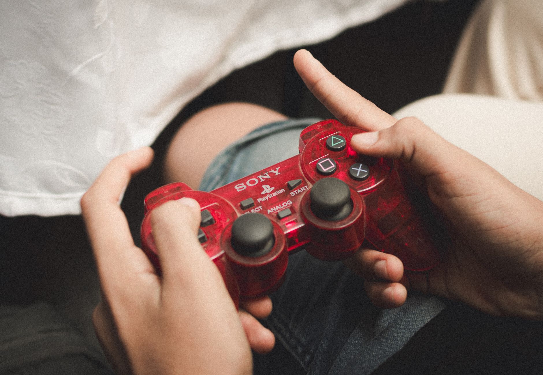 Person playing with a red PlayStation controller, evoking nostalgia for classic gaming.